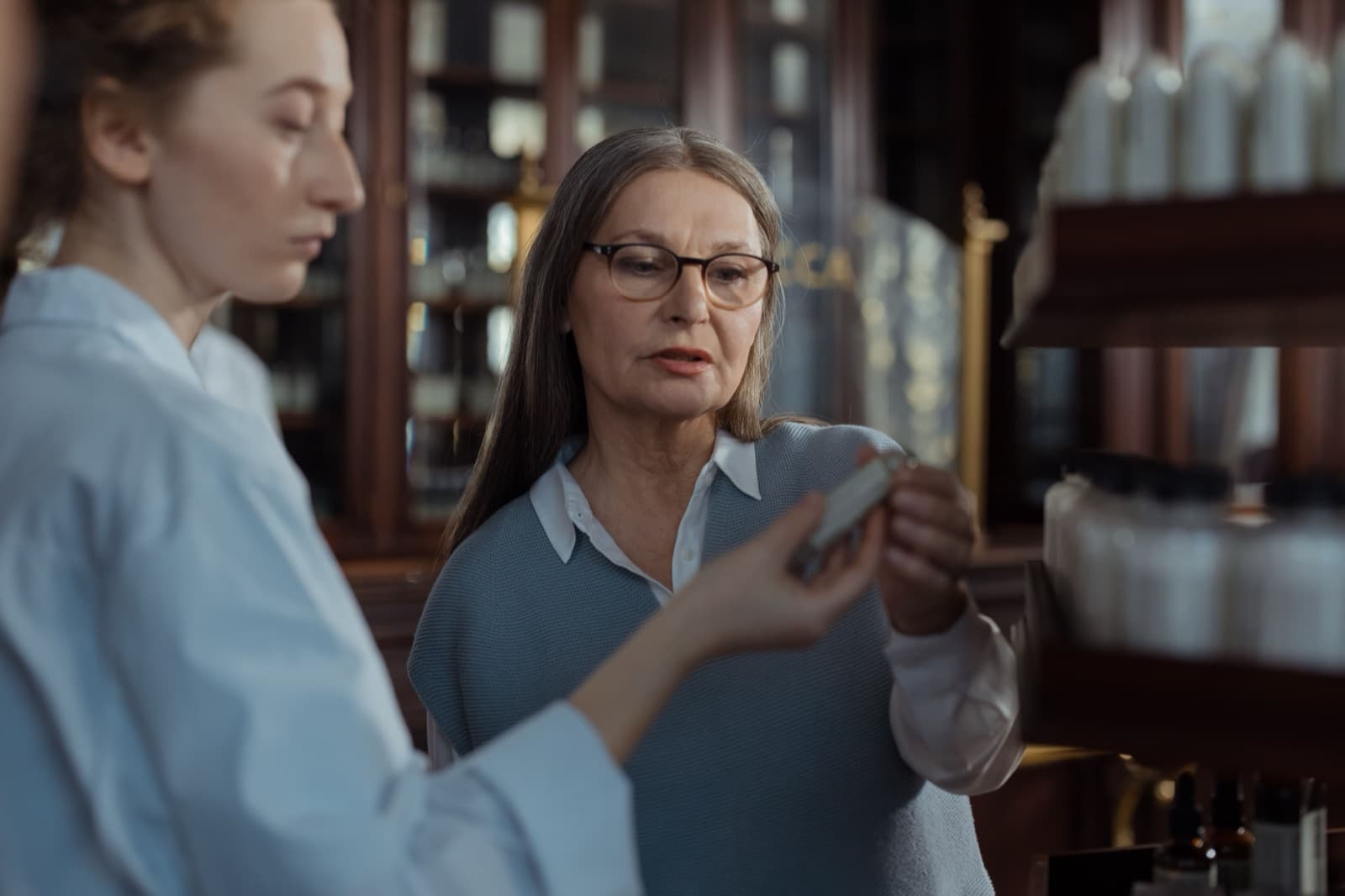 An older pharmacy customer discussing medication options with a pharmacist at the counter