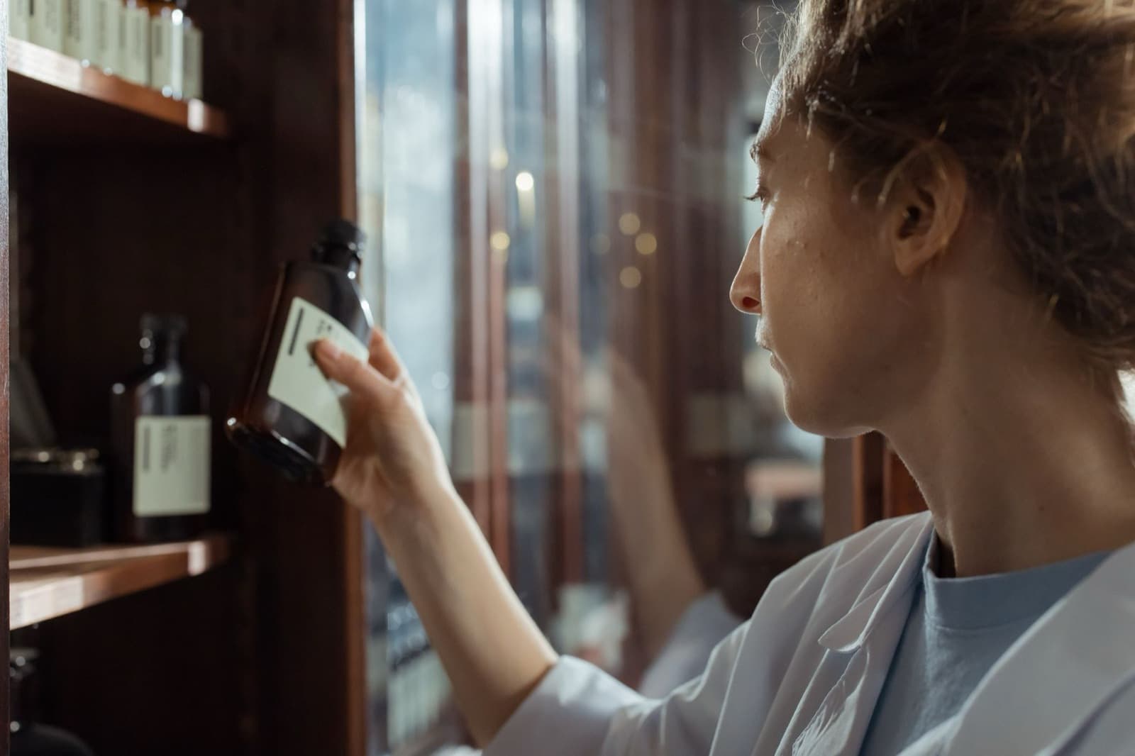 A pharmacist in a lab coat selecting a medication bottle from a pharmacy shelf